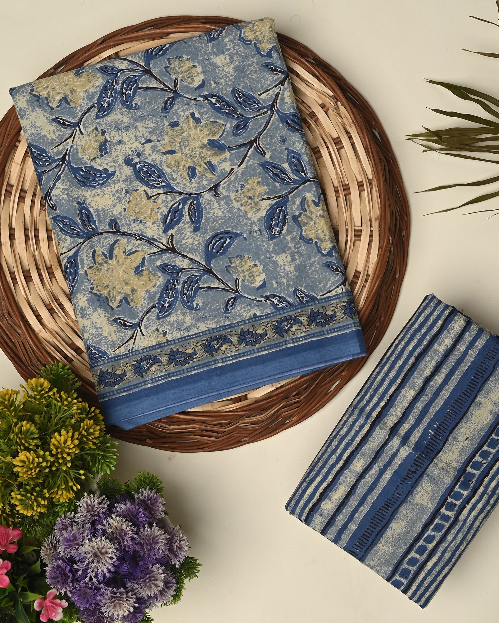 Blue floral fabric on a woven basket with striped fabric and flowers on a light background