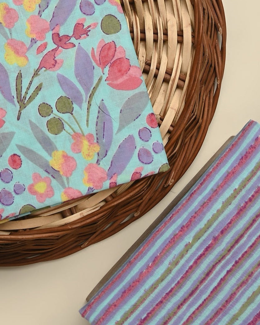Floral fabric with pink and purple flowers on a woven basket and striped fabric on a beige surface.