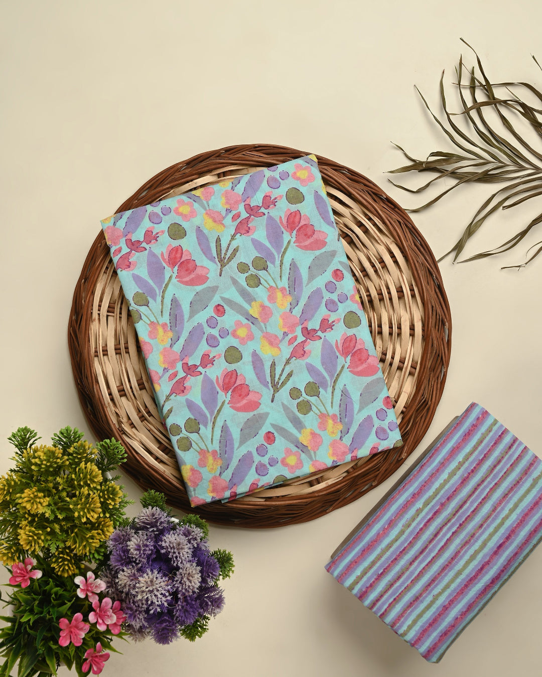 Floral-patterned notebook on a woven basket with a striped notebook and plants on a beige background